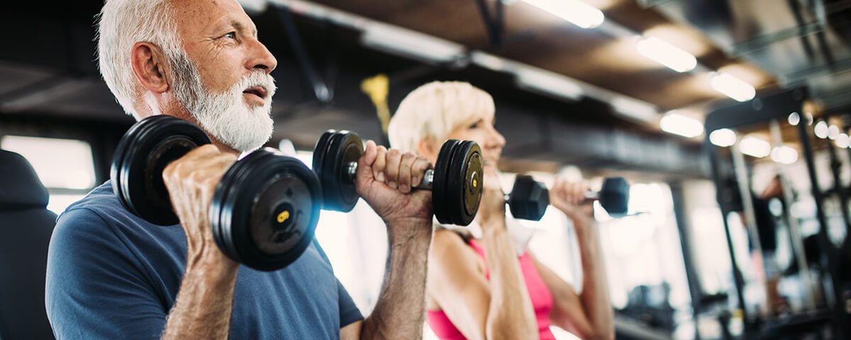 older woman and man using free weights at the gym